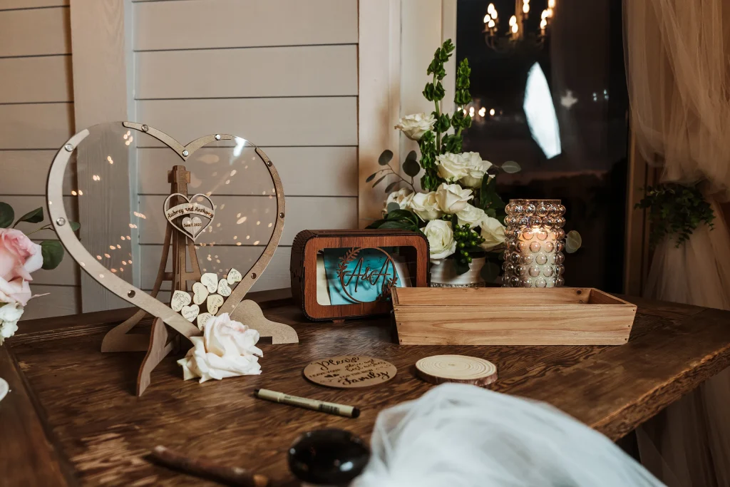 Heart-shaped wedding guest book with wooden tokens, floral arrangements, candles, and personalized d&eacute;cor displayed on a rustic table at Masters Stables.