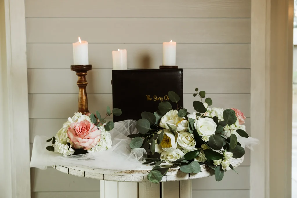 Wedding ceremony table with white and blush florals, eucalyptus greenery, lit pillar candles, and a keepsake book at Masters Stables.